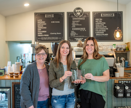 Three white females in a coffee shop holding an award