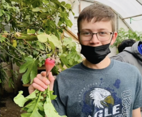 Middle school boy wearing a black facial mask holding a radish
