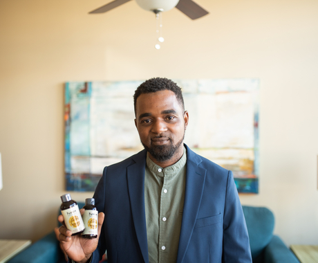 Man in a suit jacket holding two small bottles of vanilla, in a living room