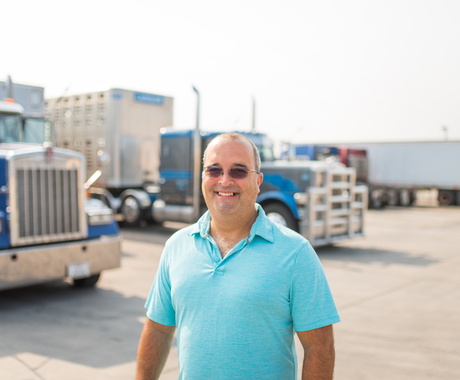 Man standing in front of two blue semis in parking lot