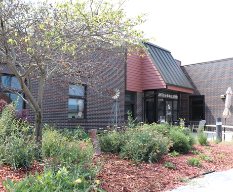 One tree and native plants surrounded by red woodchips, in front of the Center for Rural Affairs office building made with dark red bricks