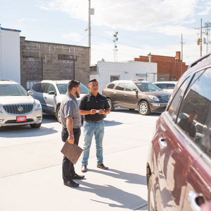 two men talking to each other while surrounded by cars