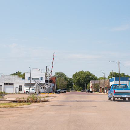 Blue pickup crossing railroad tracks into a small town main street with brick buildings on either side of the road