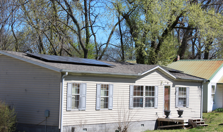 One story house, off-white house, with two separate solar panels on the roof.