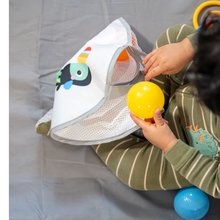 A toddler plays with balls and a bag to carry them.