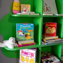 A green bookshelf contains various bilingual books in English and Spanish, and a white stuffed bear.