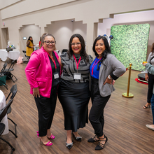 Three women posing for the camera, in a conference room