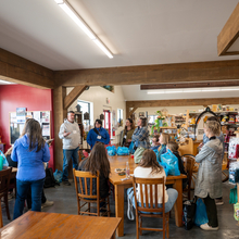 Several people gathered around tables and chairs in a small grocery store.