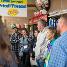 Several people stand in a small aisle of a rural grocery store conversing. 