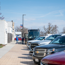 Several cars line a street and people are exiting a large black tour bus.