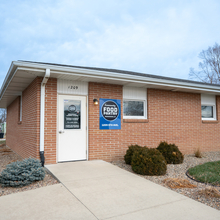 Brick house with "Community Food Pantry" posted on a blue sign with white windows and a white window.
