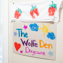 Paper sign hung on wall that says "The Wolfe Den Daycare" written with crayons