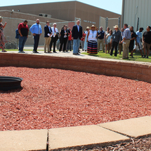 A group of people looking at a ceremonial fire pit area, round with pavers and red woodchips inside 