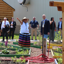 Two women, one pointing, and a man looking at a sign, standing in a garden