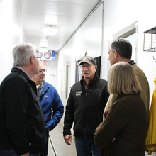 People standing in a circle in a hallway, listening to a man wearing a ball cap