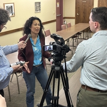 Woman speaking with two reporters, camera in the foreground