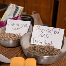 Two steel bowls are filled with prairie seed mixes on top of a wooden table