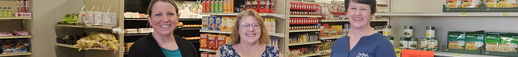 Three community leaders stand in front of grocery store shelves filed with products for sale.