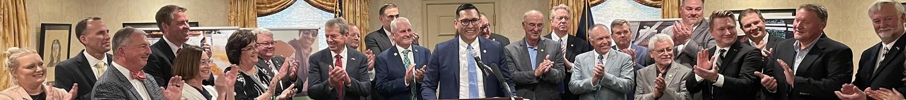 man standing at a podium with men and women in the background.