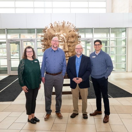 A photo of four people standing in front of a golden statue