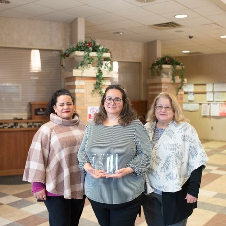 An image of three women. The center one is holding an award