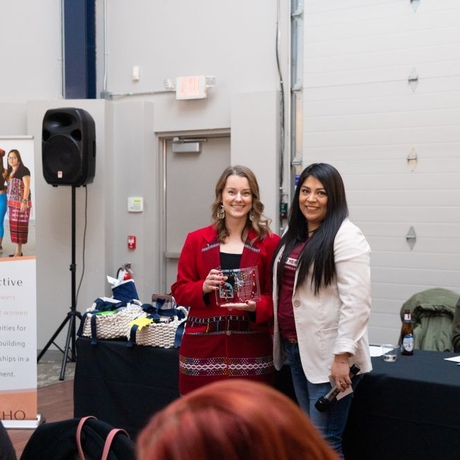 An image of two people standing with an award in front of a conference room