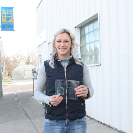 An image of a woman in a black vest holding an award