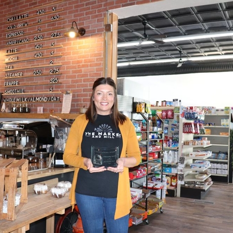 Woman in yellow cardigan standing in a storefront holding an award