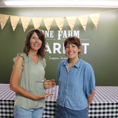Two women standing in front of a green wall and the woman in green is holding an award
