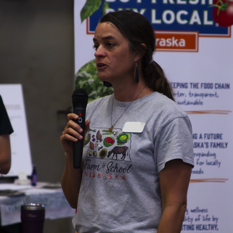 Image of a brown-haired woman in a gray shirt speaking into a microphone.