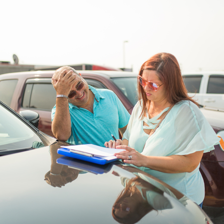 Man and woman looking at paperwork on the hood of a car