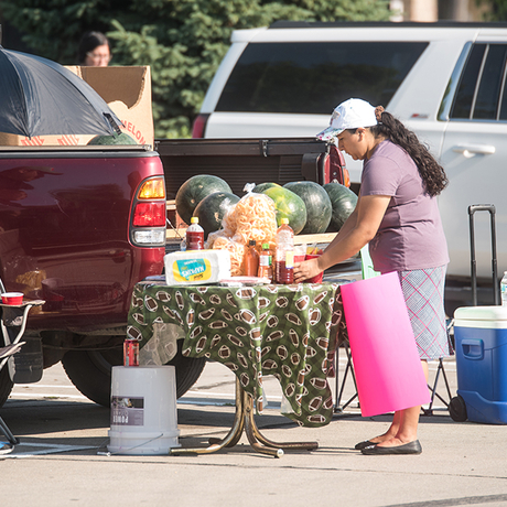 Woman places produce, including watermelon, on a table at a farmers market