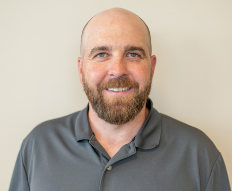 Bald man with a beard and mustache, wearing a dark colored polo shirt