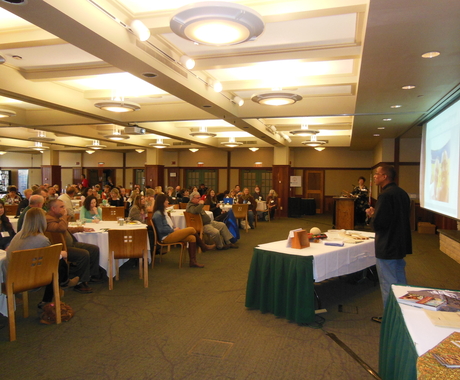 Conference with speaker at front of room, and people at tables