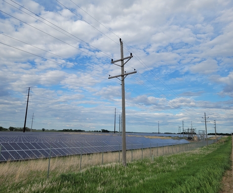 Solar panels and transmission lines in a field under a cloudy blue sky