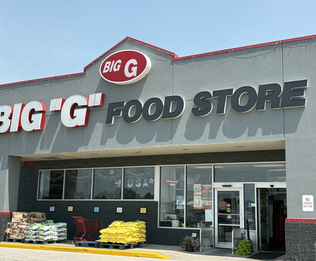 Front of a gray one-story building. Sign says "Big 'G' Food Store. Below the sign are large windows and two glass doors.
