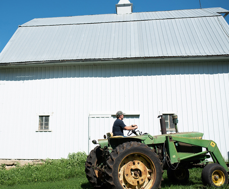 Farmer on a tractor with a building in the background.