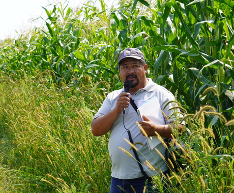Man speaking into microphone with corn in the background