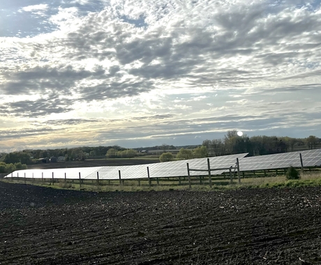 Solar arrays with farmland in the foreground and beautiful cloudy sky with tones of yellow and blue in the sky