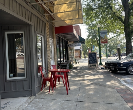 red table and chairs sitting outside main street buildings with a black car parked on the street.