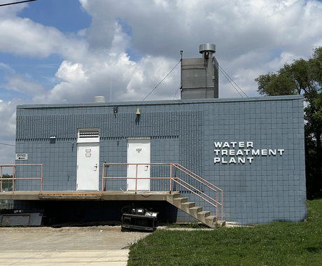 A one-story blue bricked building with two white doors. White lettering on the building says "Water Treatment Plant"