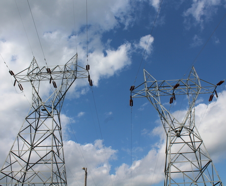 Looking up at transmission towers under a cloudy blue sky