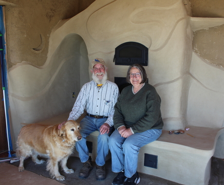 Hombre y mujer sentados en una chimenea de arcilla con un perro dorado parado frente a ellos