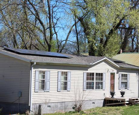 Casa de un piso de color blanquecino con dos paneles solares en el techo