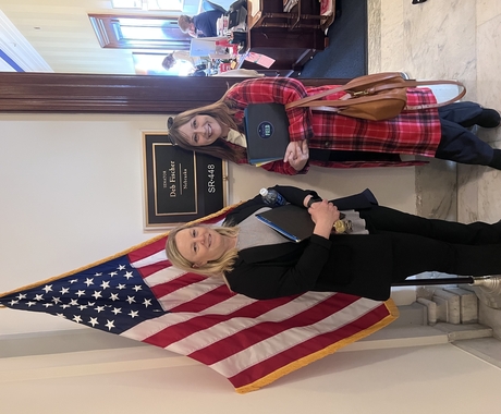 Two women standing in front of a placard outside of an office that says "Deb Fischer Nebraska" and an American Flag.