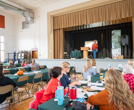 Local Foods Summit group photo. Speaker on a stage with people listening at tables below.