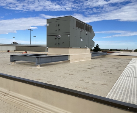Aire acondicionado y calefacción en la azotea de un edificio con tejado plano. Cielo azul con nubes tenues al fondo.