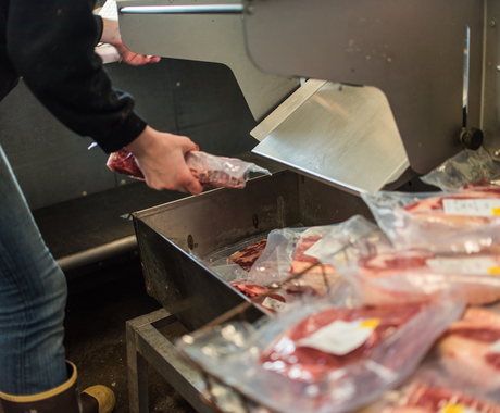 a person picking up a package of meat from a machine, with packages of meat on a table nearby