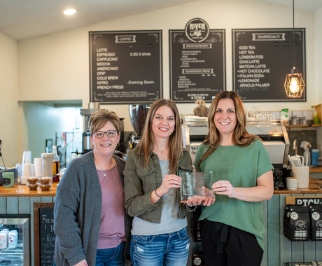 Tres mujeres blancas en una cafetería se toman una foto con un premio en mano
