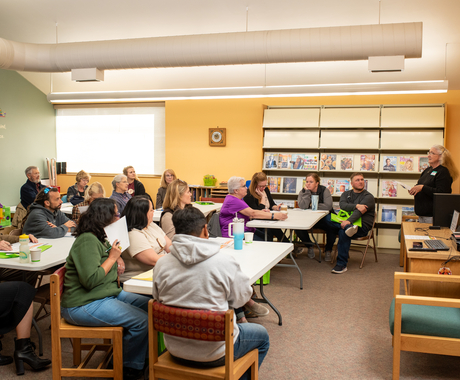 A group of people sitting at tables and a woman standing talking.